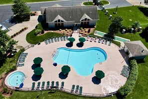 Une grande piscine, dotée de chaises longues et de parasols, entourée d’une pelouse bien entretenue et d’un bâtiment dont le toit est en pente.