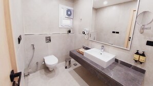 Une salle de bain moderne avec des toilettes blanches, un grand miroir et un comptoir en marbre.
