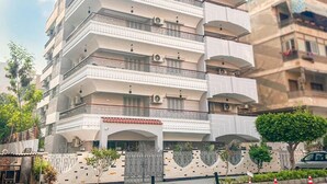 Un immeuble résidentiel à plusieurs étages, doté de balcons, de climatiseurs et d’une entrée sécurisée par un portail.