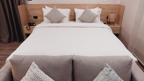 Une chambre d’hôtel avec une tête de lit en bois, un grand lit avec une literie blanche, deux tables de chevet avec des lampes et une vue sur l’intérieur de la pièce.