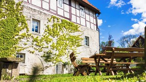 A traditional half-timbered building with ivy-covered walls, a wooden bench, and a grassy lawn. - Vacation in the castle up to 15 pers. Apartment: Burggraf & Himmelsleiter (Großbodungen)