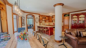 A spacious living room with a wooden dining table, a leather sofa, and a kitchen area with wooden cabinets and a red island.