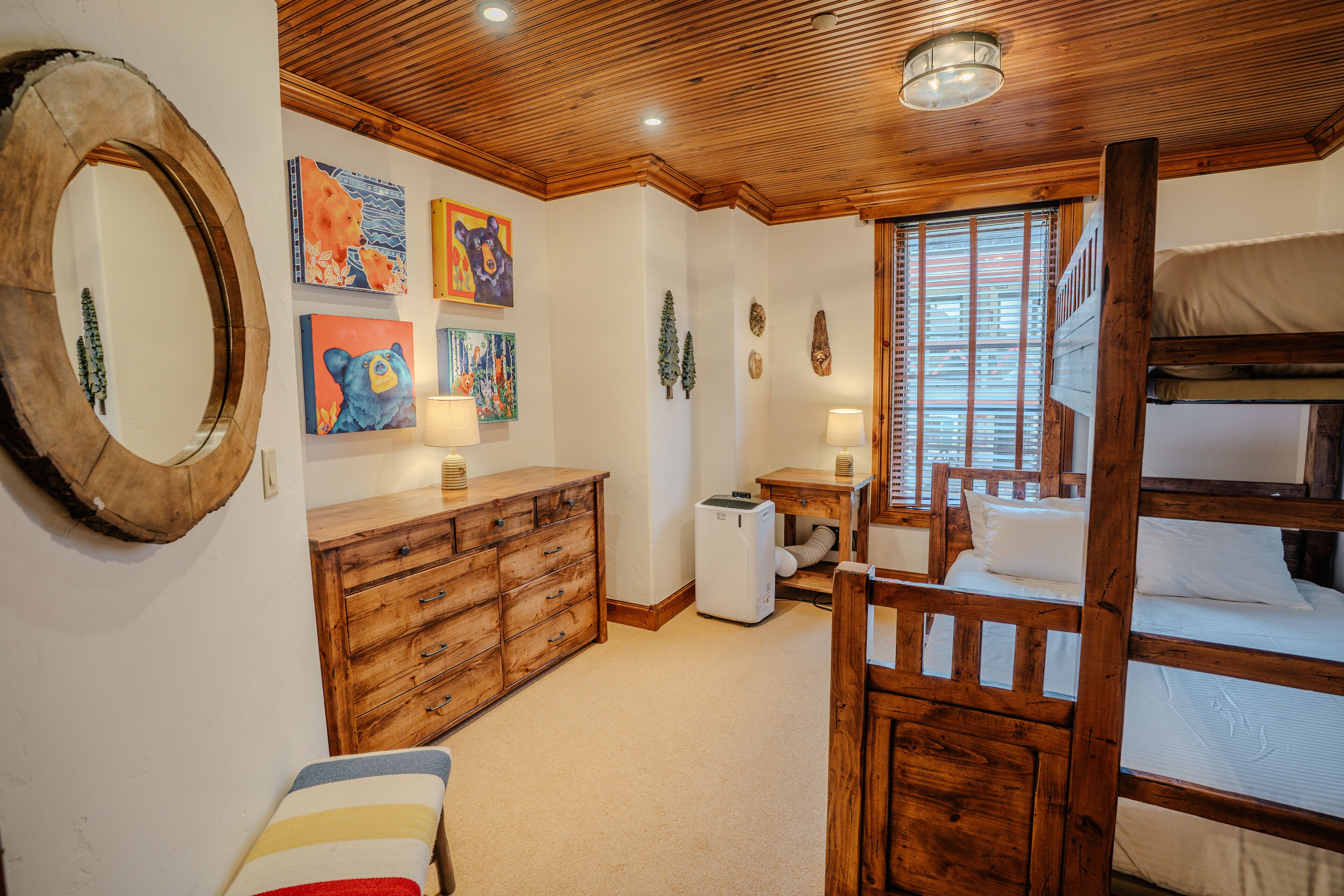 Ein Schlafzimmer mit Etagenbett, Holzkommode und Wandbildern.