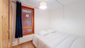 A bedroom with a wooden door, a window with curtains, a bed with white bedding, and a ceiling light.