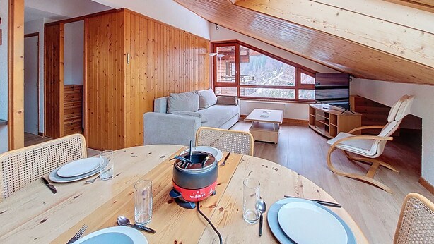 A cozy, wooden interior with a dining area, a sofa, and a view through large windows.