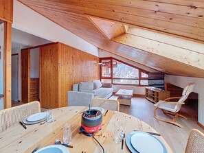 A cozy, wooden interior with a dining area, a sofa, and a view through large windows.