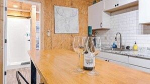 Una cocina con armarios blancos, encimera de madera y una botella de vino con copas.