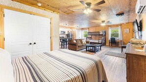 Una habitación con una cama, un sofá, una mesa de comedor, un ventilador de techo y una zona de cocina al fondo.