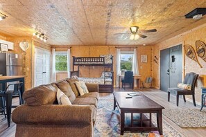 Interior rústico de una cabaña con techo de madera, una litera, un sofá, una mesa de comedor y una zona de cocina.