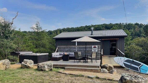Una terraza de madera con mobiliario exterior, un jacuzzi y una tabla de surf.
