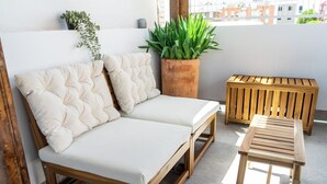 A wooden sofa with white cushions and a matching bench on a balcony.