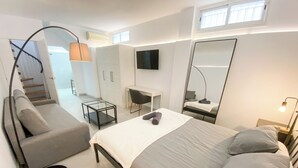 A modern bedroom with a bed, a sofa, a desk, and a TV.