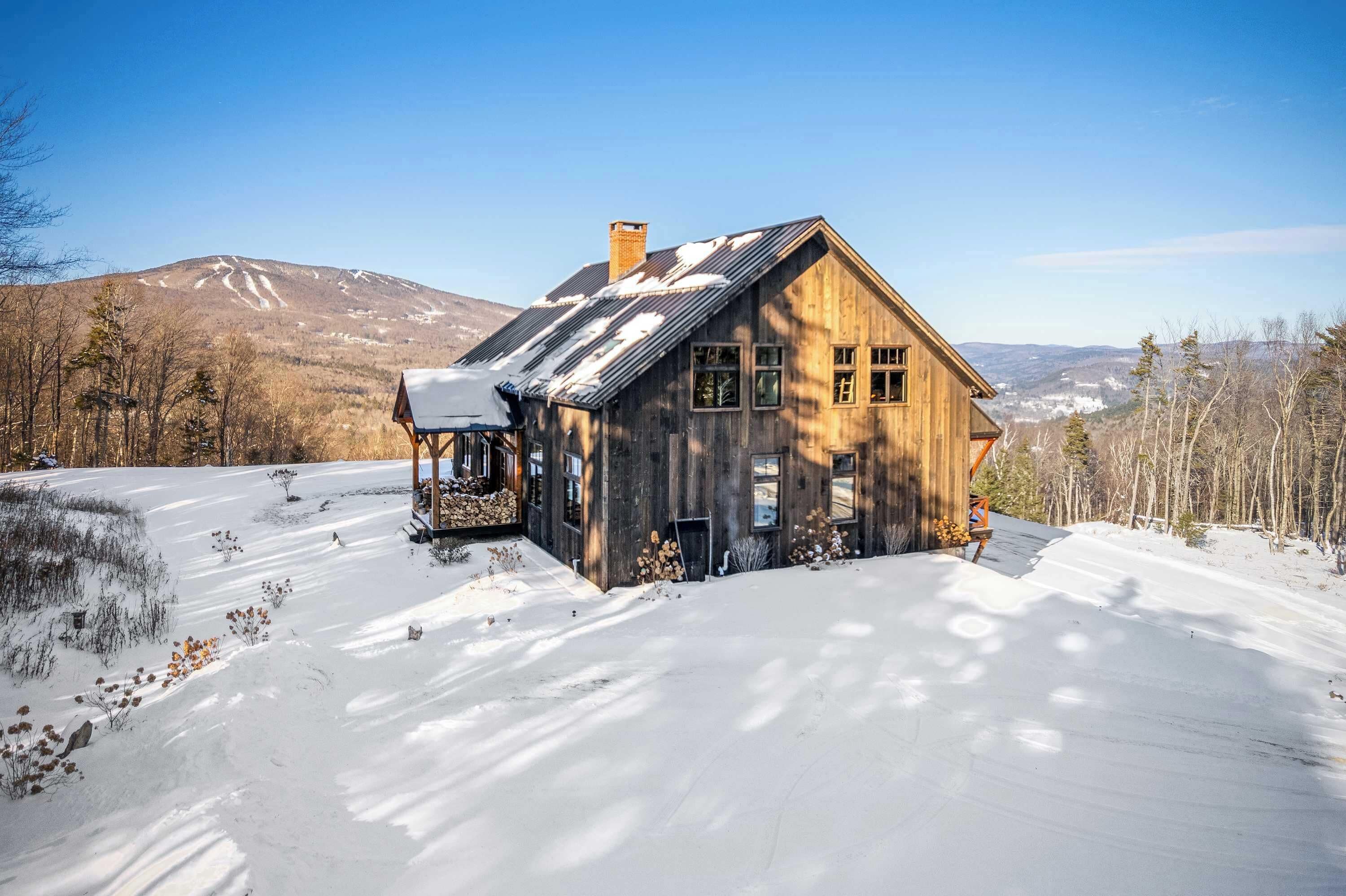 Une cabane en bois, dotée d’un toit en pente, entourée d’un paysage enneigé et d’arbres, avec une montagne en arrière-plan.