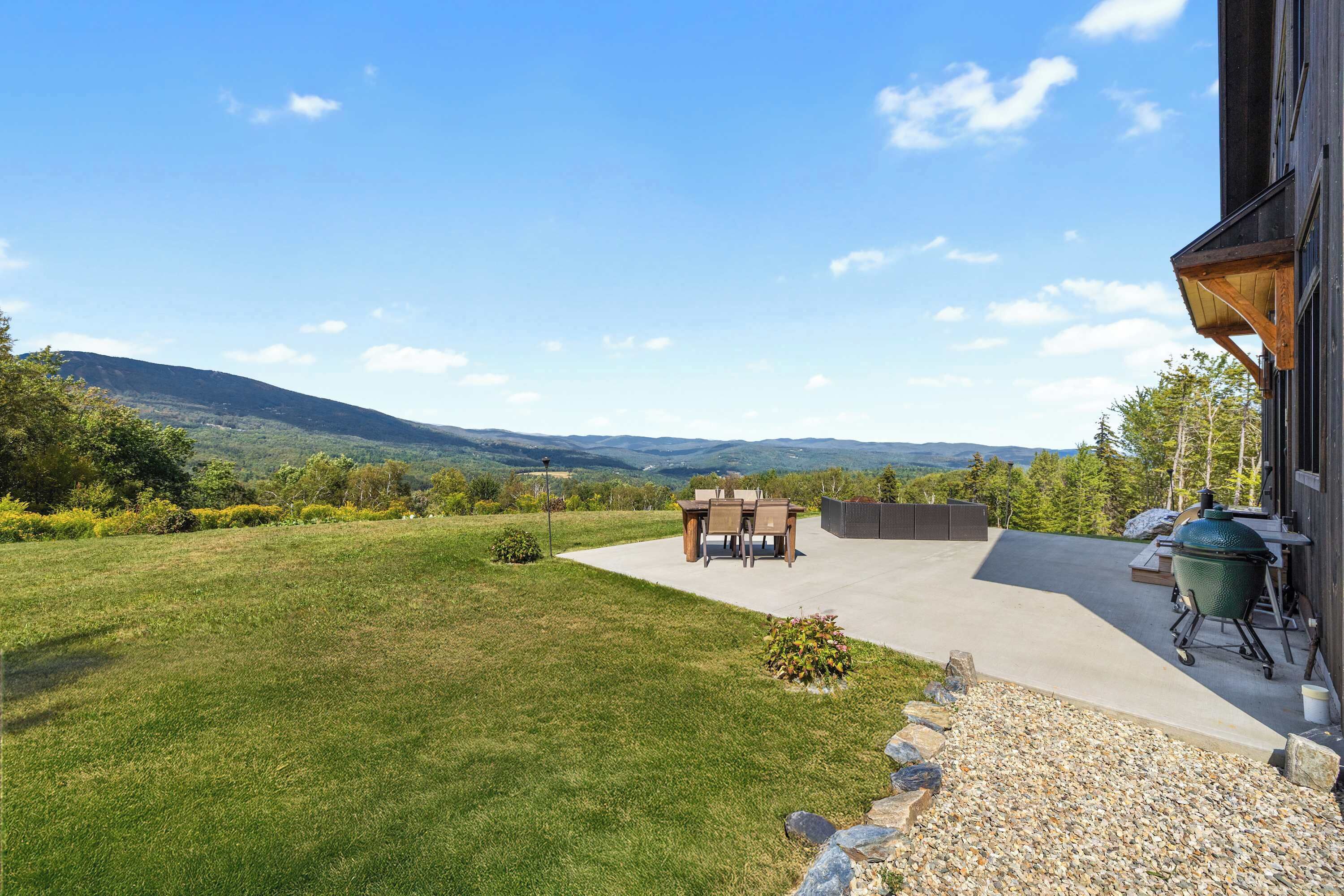 A patio with a view of mountains, a barbecue grill, and a dining table with chairs.