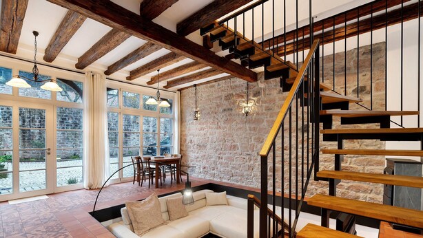 A modern interior with a stone wall, wooden staircase, and a white sofa in a spacious room with large windows.
