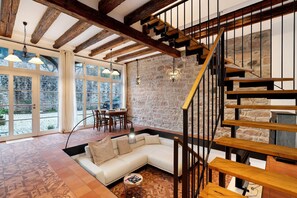 Un intérieur moderne avec un mur en pierre, un escalier en bois et un canapé blanc dans une pièce spacieuse dotée de grandes fenêtres.