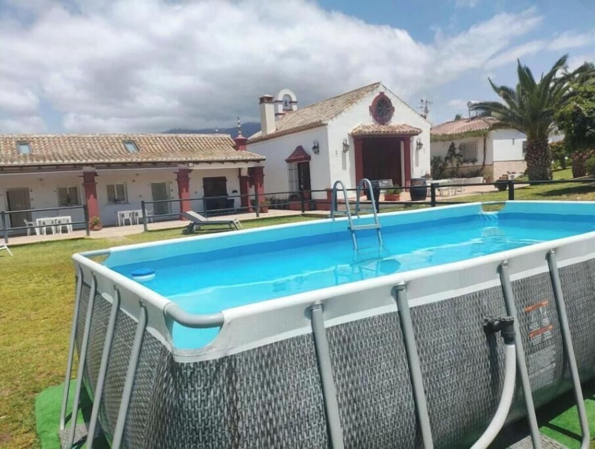 Une piscine avec un escalier, entourée d’une pelouse et bordée d’un bâtiment dont le toit est recouvert de tuiles.