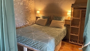 A bedroom with a stone wall, a wooden bed frame, two bedside tables with lamps, and a wooden ladder shelf.