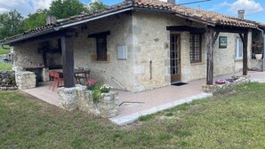 A stone house with a tiled roof, a wooden door, and a small porch with a table and chairs.