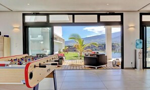 Un interior moderno con mesa de fútbol, zona de estar con vistas a un jardín ajardinado y montañas.