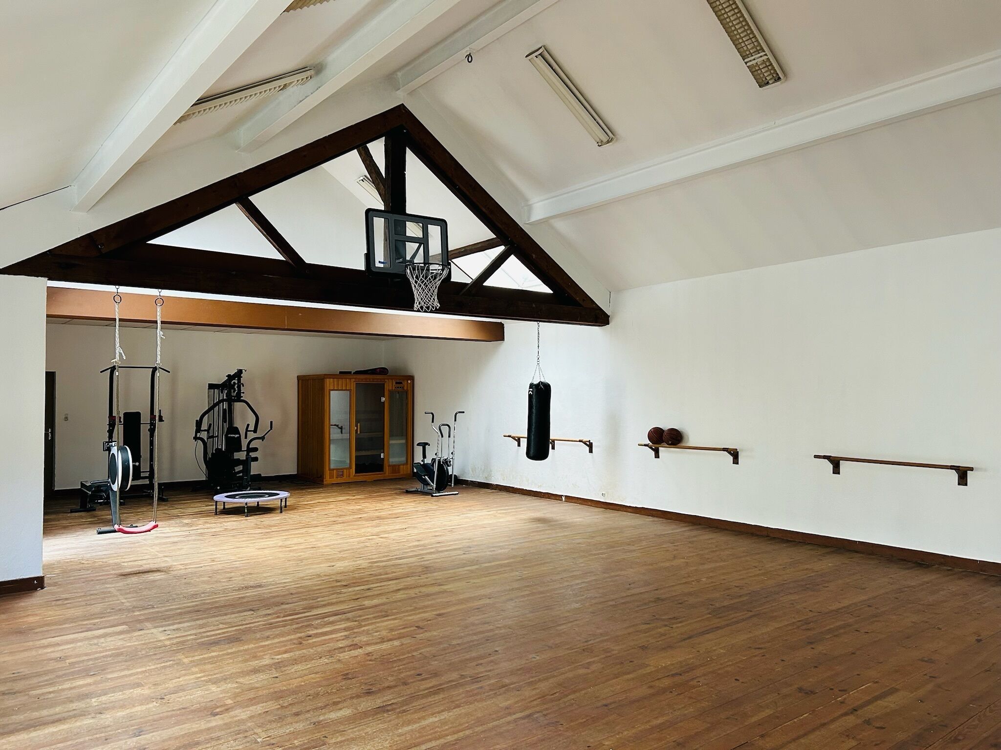 Una habitación amplia con techo alto, vigas de madera, aro de baloncesto y equipo de ejercicio.