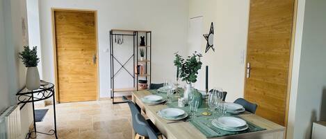 A dining area with a wooden table set for four, flanked by two wooden doors, a black metal shelf unit, and a potted plant.