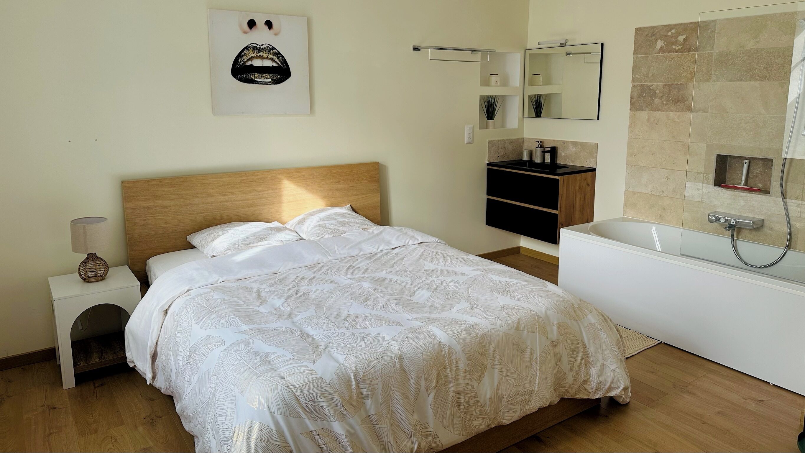 A bedroom with a bed, bedside table, lamp, and a bathroom with a bathtub and shower.