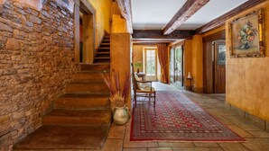 Un escalier en pierre menant à une porte en bois, un tapis rouge à motifs et un tableau accroché au mur.