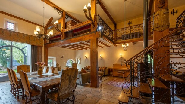 Un vaste espace dédié à la salle à manger, avec une table et des chaises en bois, un escalier doté de rampes en fer forgé et une vue sur l’extérieur grâce à de grandes fenêtres.