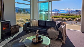 A modern living room with a large window, a fireplace, and a view of mountains and a lake.