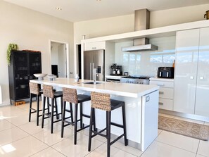A modern kitchen with a central island, bar stools, a coffee machine, and a stove.