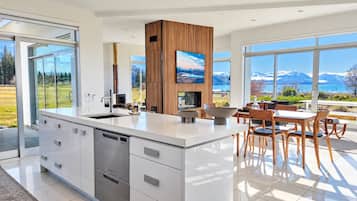 A modern kitchen with a large island, a dining area with wooden chairs, and a view of mountains through large windows.