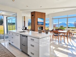 A modern kitchen with a large island, a dining area with wooden chairs, and a view of mountains through large windows.