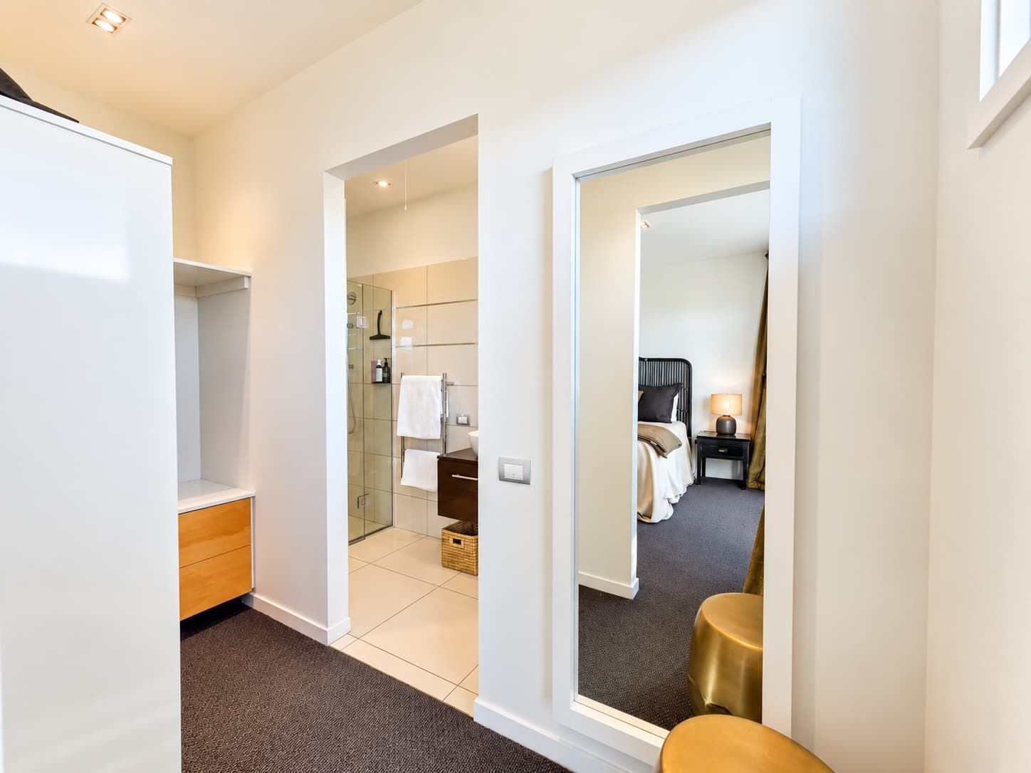 A hotel room with a walk-in closet, a bathroom with a glass shower, and a bed with a nightstand.
