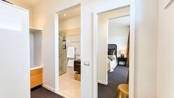 A hotel room with a walk-in closet, a bathroom with a glass shower, and a bed with a nightstand.