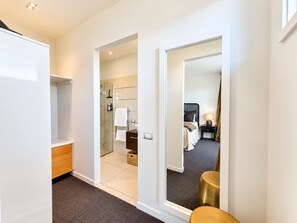 A hotel room with a walk-in closet, a bathroom with a glass shower, and a bed with a nightstand.