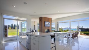 A modern kitchen with a large island, white cabinetry, and a view of a mountainous landscape through large windows.