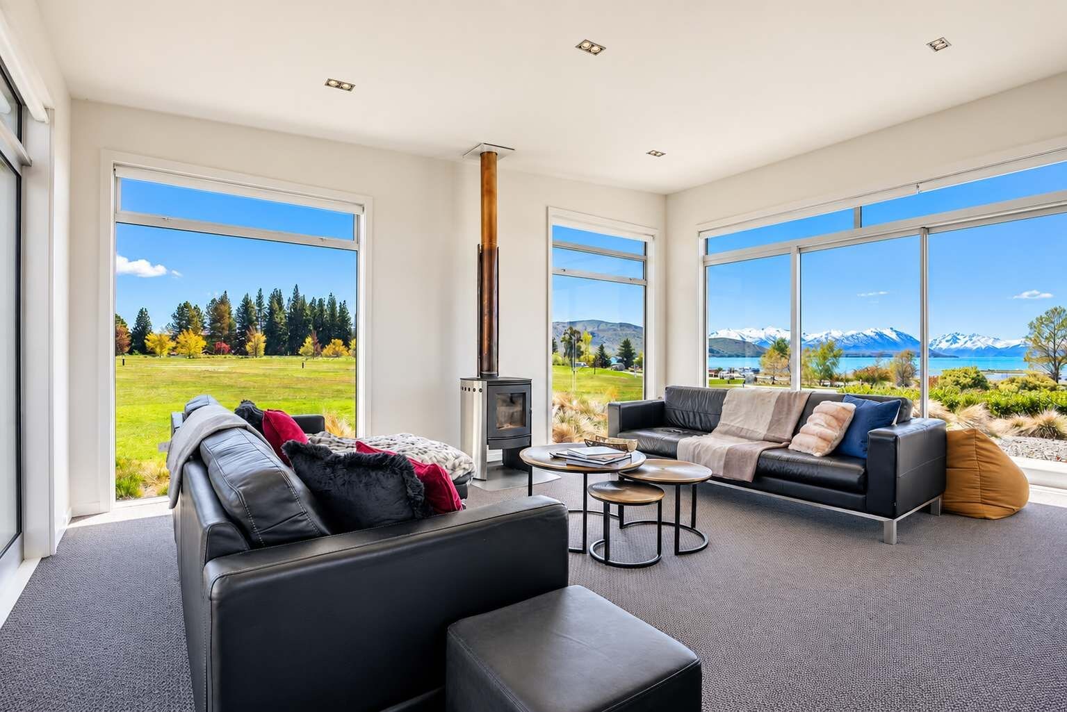 A modern living room with a fireplace, large windows, and a view of mountains and a lake.
