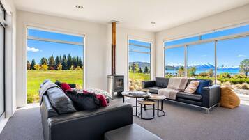 A modern living room with a fireplace, large windows, and a view of mountains and a lake.