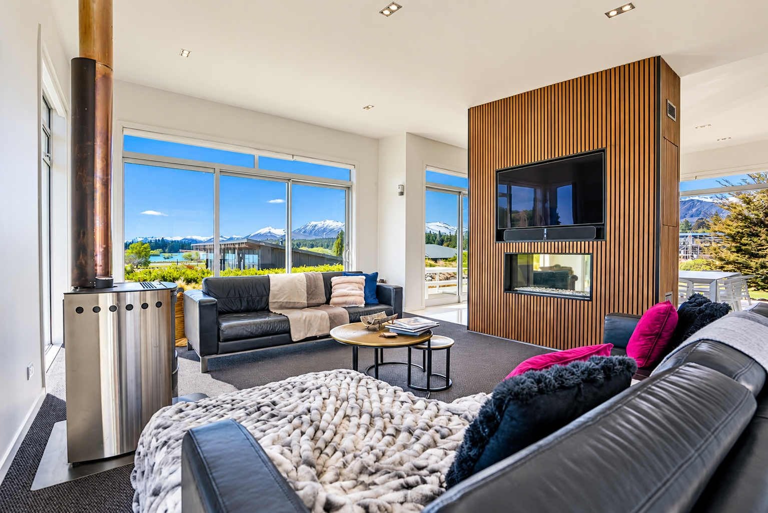 A modern living room with a fireplace, a sofa, a coffee table, and a TV mounted on a wooden wall.
