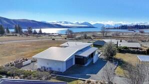 A modern house with a sloped roof, located near a lake with mountains in the background.