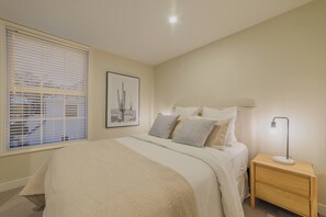 Un dormitorio con cama, mesita de noche, lámpara y ventana con persianas.