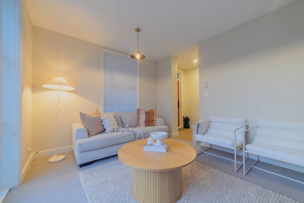 A modern living room with a sofa, two white chairs, a round coffee table, a floor lamp, and a ceiling light.