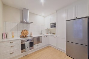A modern kitchen with white cabinetry, stainless steel appliances, and a wooden cutting board on the countertop.