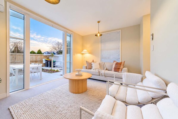 A modern living room with a sofa, a coffee table, and a view of the backyard.