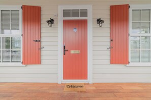 Una casa con puerta roja, contraventanas blancas y felpudo.