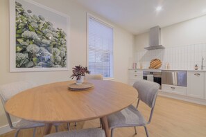 Un comedor con una mesa redonda de madera, sillas tapizadas en gris, una planta en maceta y una obra de arte floral grande enmarcada en la pared.