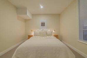 A bedroom with a bed, two bedside tables with lamps, a wall-mounted artwork, and a window with blinds.