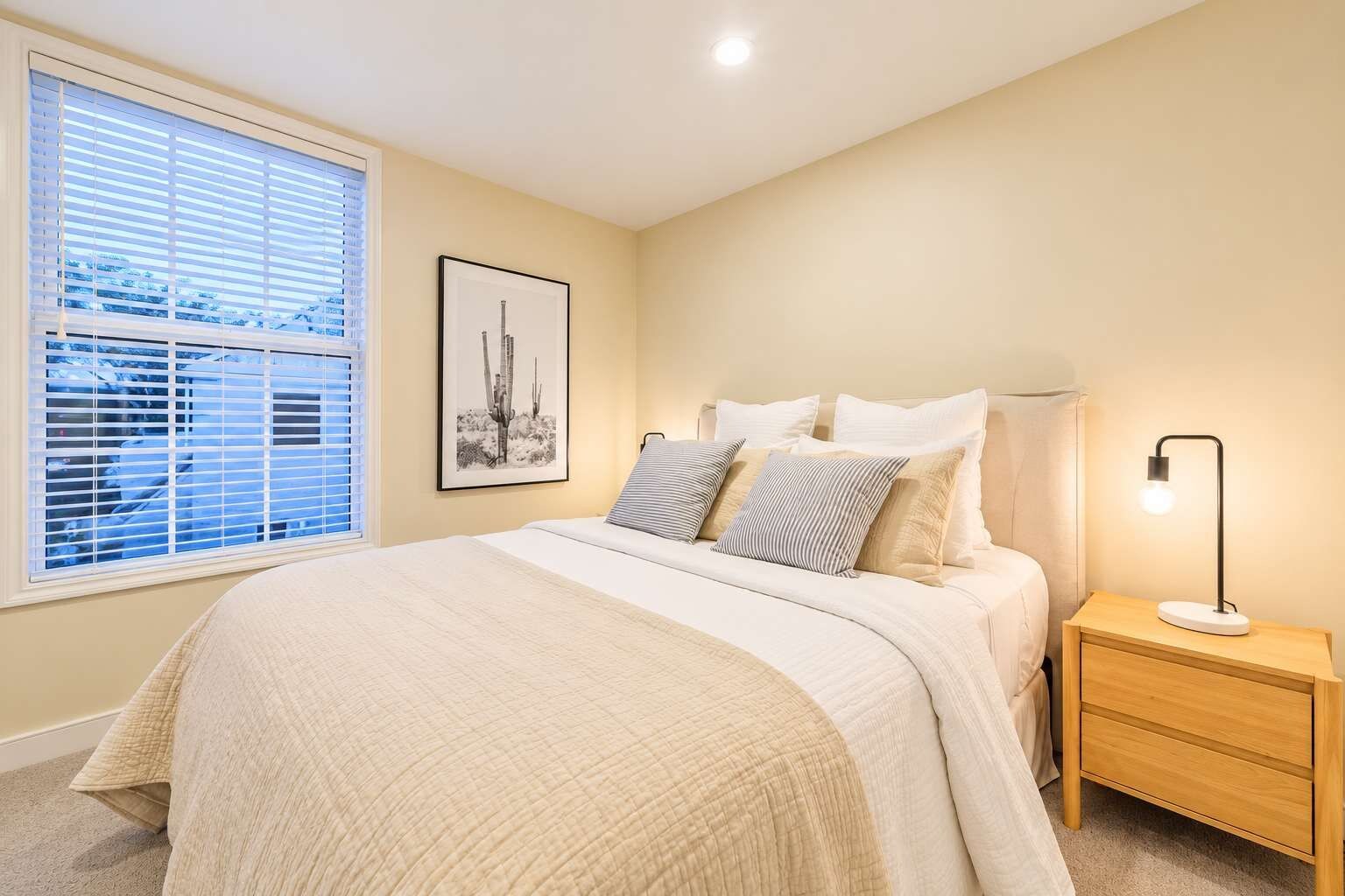 Un dormitorio con cama, mesita de noche, lámpara y ventana con persianas.