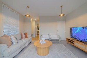 A modern living room with a white sofa, a round coffee table, and a flat-screen TV.